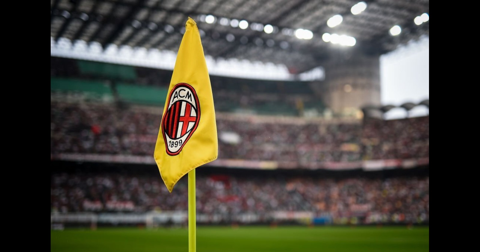 Bandeira do AC Milan no estádio durante uma partida, com ampla torcida ao fundo. Um símbolo do futebol italiano e da parceria com o melhor cassino que paga em criptomoedas