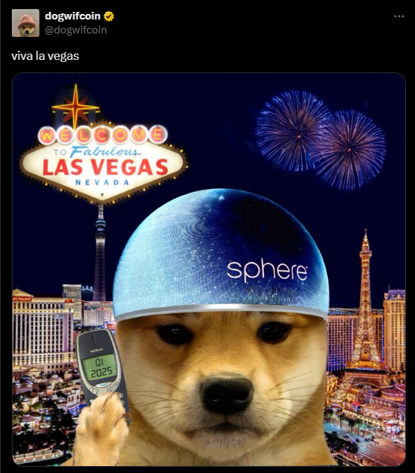 A imagem apresenta uma montagem divertida com um cão da raça Shiba Inu, que possui uma expressão curiosa e vestindo um capacete azul com a palavra "sphere" estampada. O fundo exibe o famoso letreiro de "Welcome to Fabulous Las Vegas" iluminado, com fogos de artifício no céu, complementando a celebração. O cão segura um celular antigo que exibe a data "01/2025". Acima, o tweet diz: "viva la vegas", celebrando a cidade de Las Vegas de maneira humorística e leve.