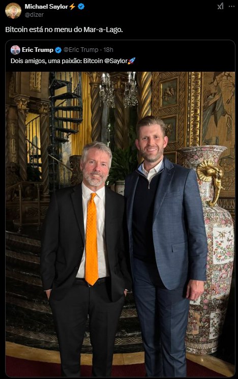 A imagem mostra Michael Saylor, CEO da MicroStrategy, e Eric Trump, filho do ex-presidente Donald Trump, em um ambiente luxuoso dentro da propriedade Mar-a-Lago. Saylor está vestido com um paletó escuro e uma gravata laranja, enquanto Eric Trump usa um paletó azul e uma camisa branca. Ao fundo, há uma decoração rica com elementos dourados e uma grande jarra ornamental. Ambos estão sorrindo e posando lado a lado, evidenciando um momento de camaradagem e entusiasmo pelo Bitcoin.