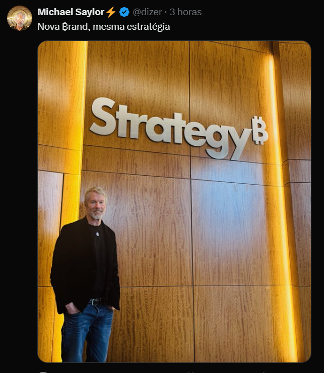 O tweet de Michael Saylor, CEO da Strategy (anteriormente MicroStrategy), destaca a recente mudança de nome da empresa para "Strategy", que reflete sua nova identidade, enquanto mantém a mesma estratégia de acumulação de Bitcoin. Na imagem, Saylor aparece ao lado de uma parede de madeira clara com o nome "Strategy" em letras grandes e brancas, incorporando o símbolo de Bitcoin. Ele está vestido com uma camisa preta e um blazer escuro, sorrindo de forma confiante. A iluminação suave e o fundo simples ressaltam a modernidade e o profissionalismo da nova marca, sinalizando um compromisso contínuo com a inovação em Bitcoin e inteligência artificial.